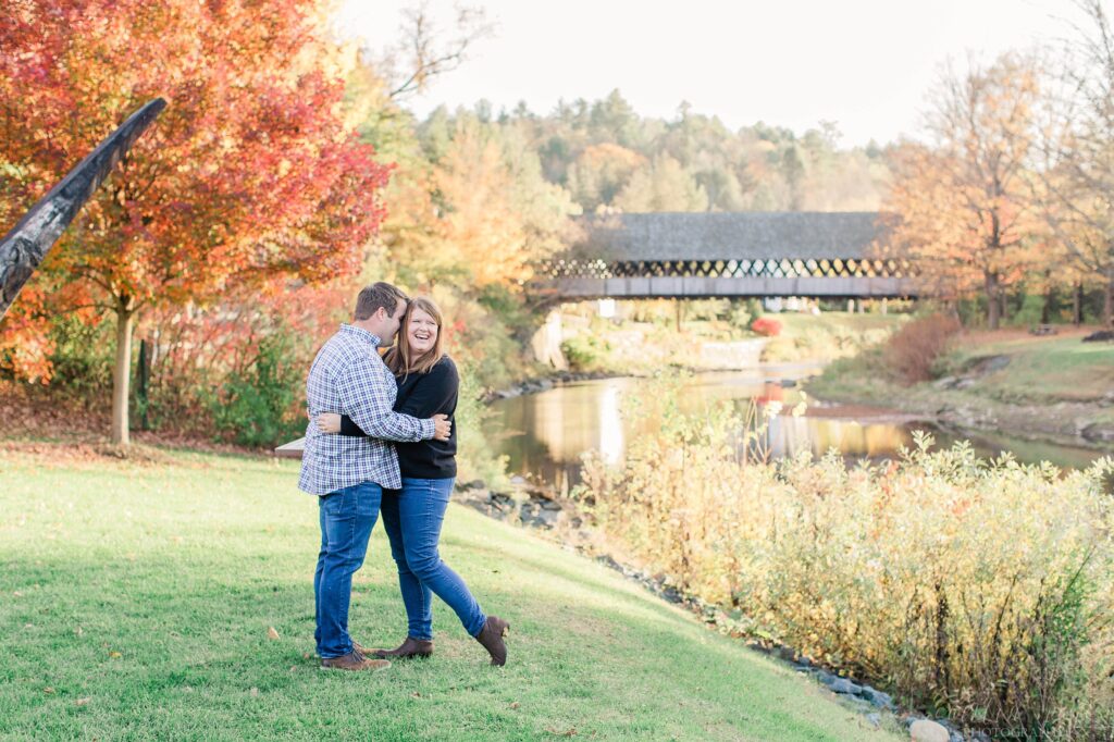 Couple standing together in field in front of Woodstock covered bridge
