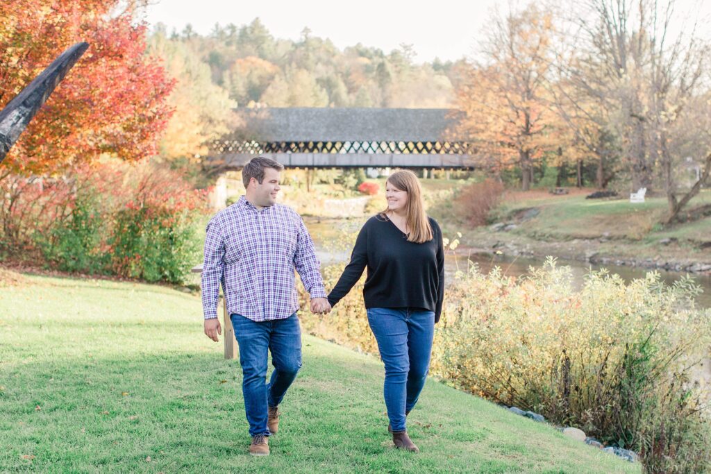 Couple walking together in field in front of Woodstock covered bridge