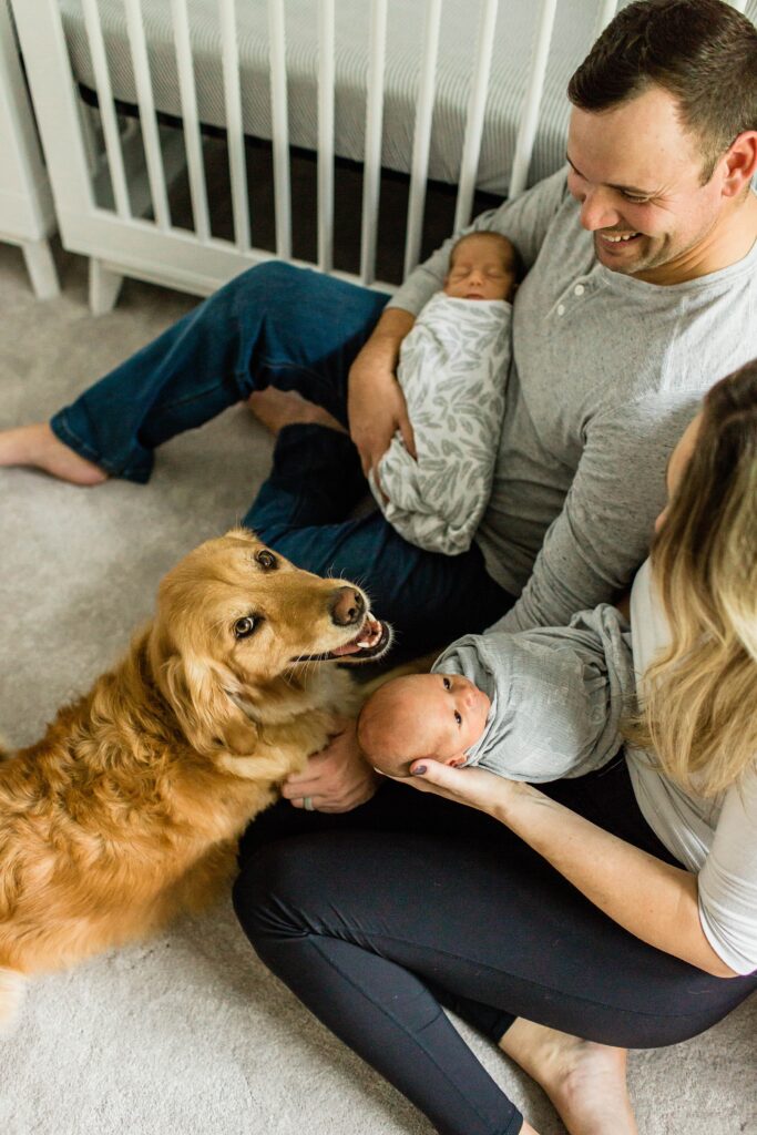 Mom and dad holding twin babies in nursery with dog
