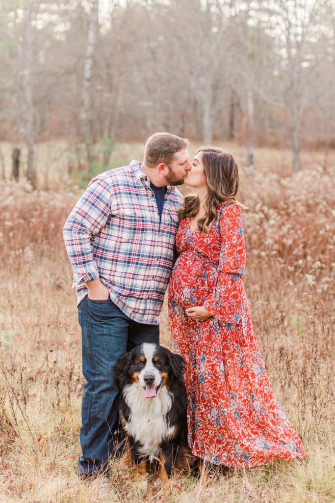Couple kissing with bernese mountain dog standing together in a field