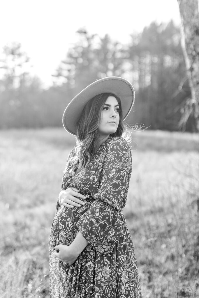 Black and white photo of pregnant woman standing in a field at sunset