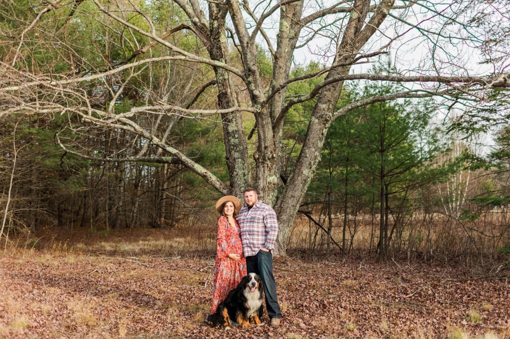 Couple standing with bernese mountain dog under large oak