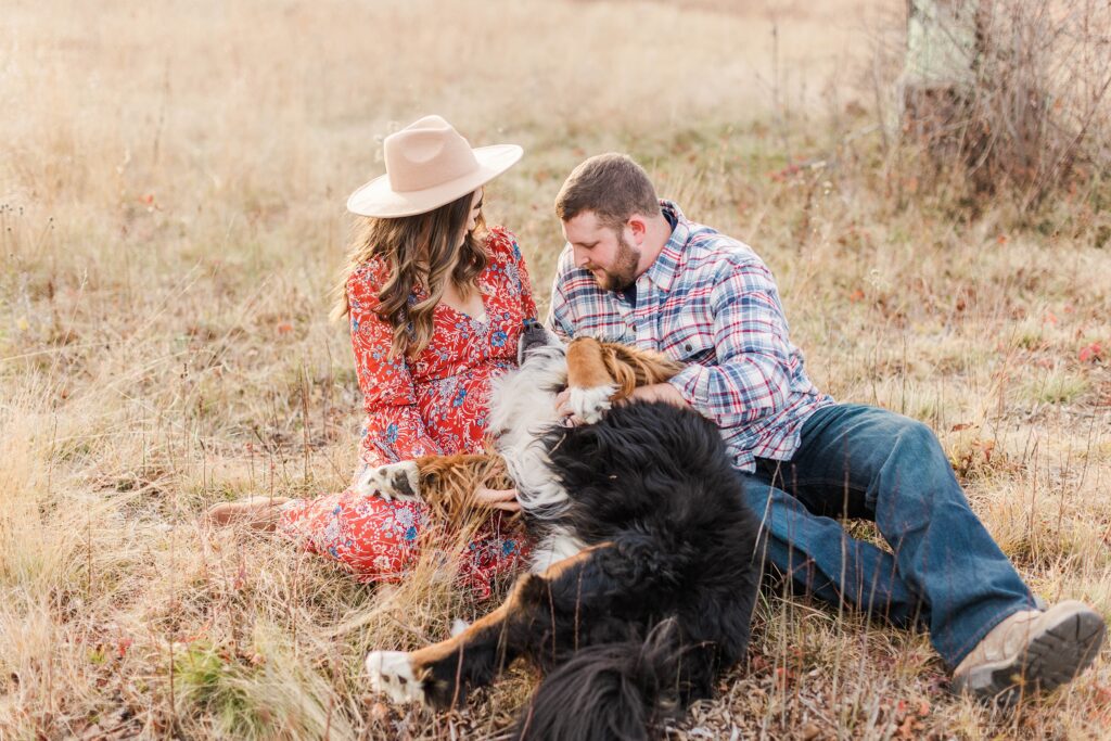 Couple sitting in field with bernese mountain dog