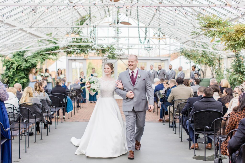 Bride and groom walking back down the aisle together in greenhouse