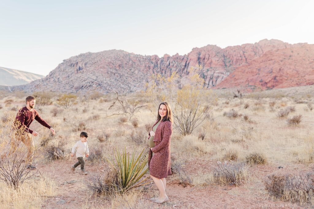 Pregnant woman standing in desert with toddler running to her