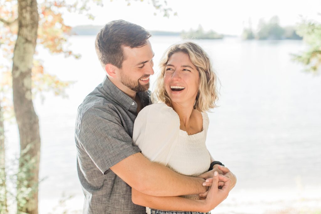 Man and woman laughing while snuggled together in front of the lake