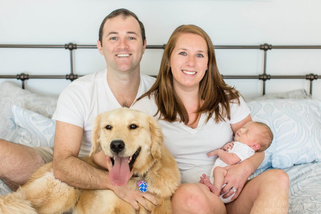 Golden retriever sitting on bed with parents and newborn baby