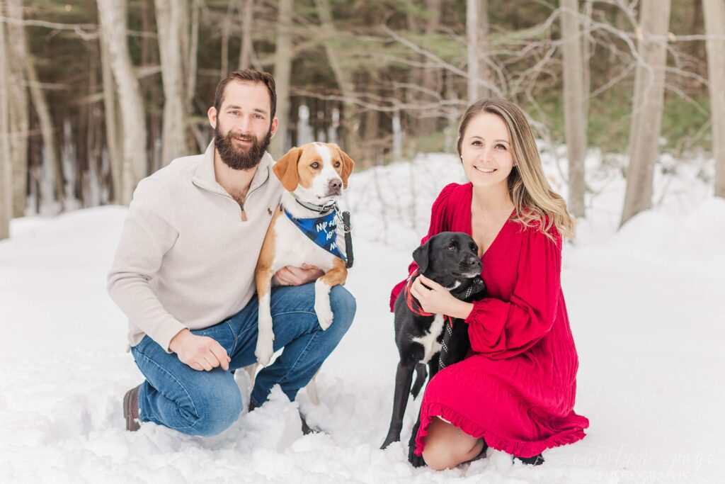 Couple sitting in the snow with their two dogs