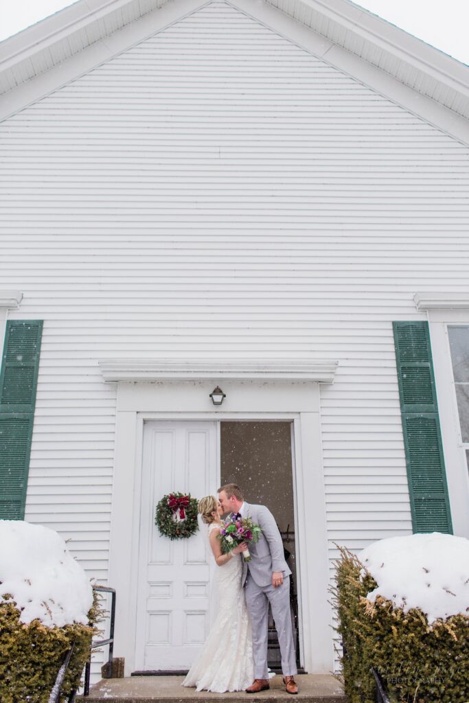 Bride and groom standing in the snow outside of church
