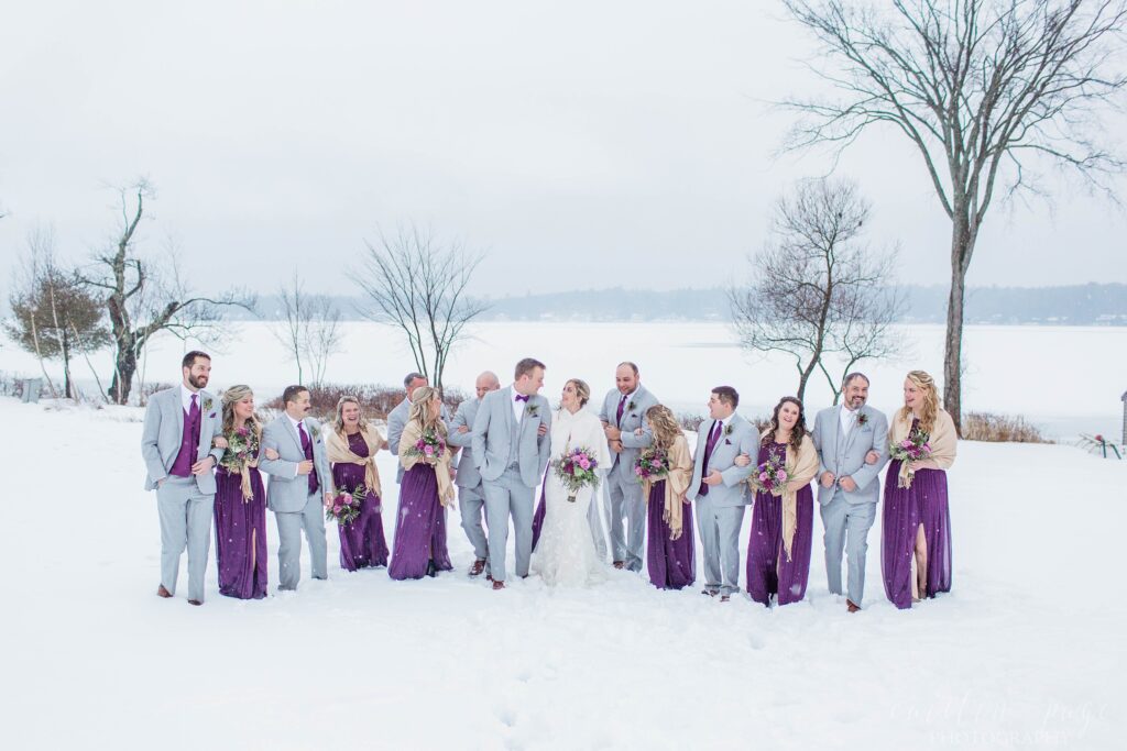 Bridal party and couple standing in the snow in front of frozen lake