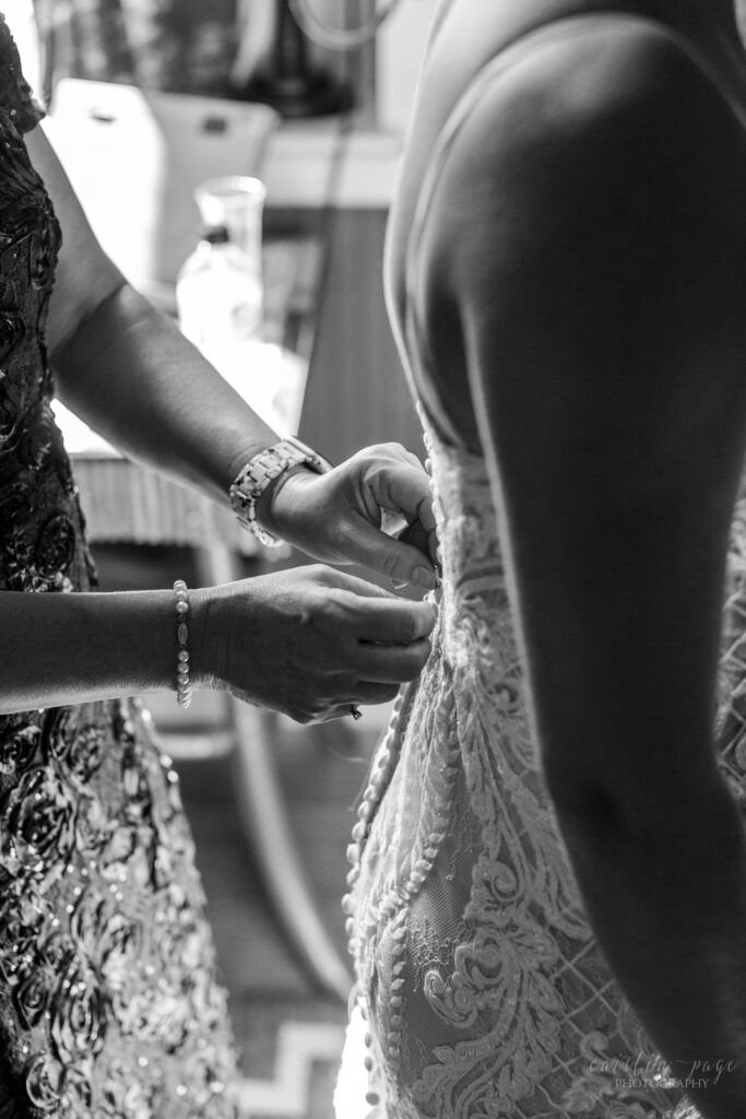 Black and white image of mom buttoning up brides dress