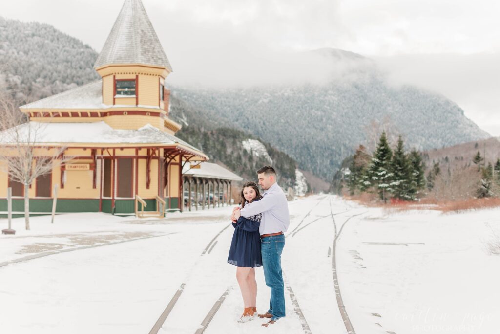Couple standing next to old train station in the snow