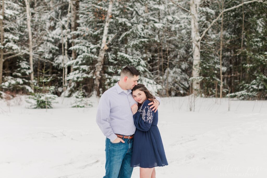 Couple snuggled together in front of snowy trees