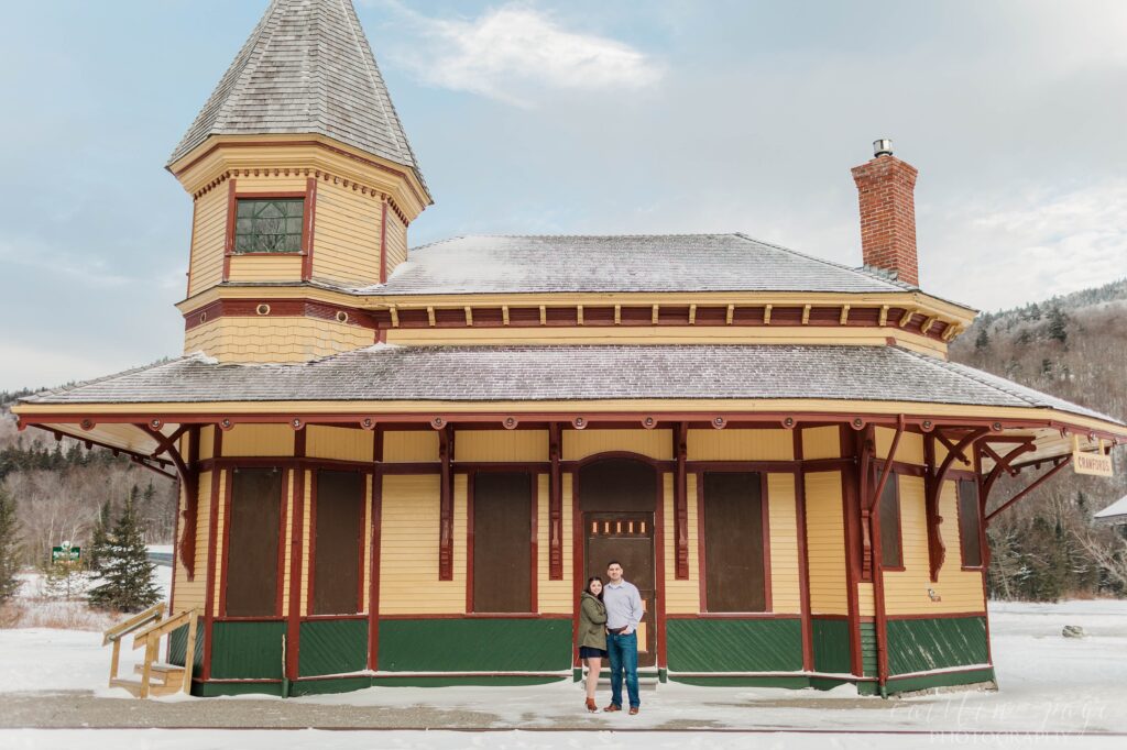 Couple standing in front of old train station in the snow