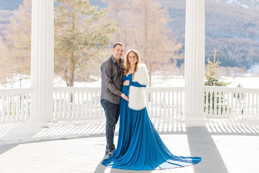 Pregnant woman in blue dress standing on balcony with man