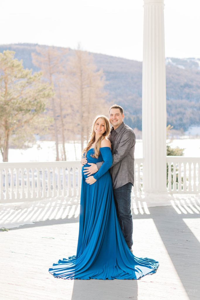 Pregnant woman in blue dress standing on balcony with man
