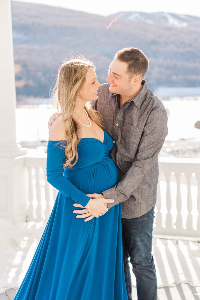 Pregnant woman in blue dress standing on balcony with husband