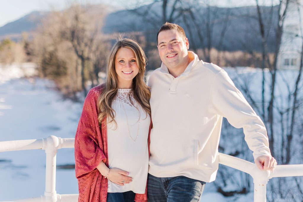 Pregnant woman and husband standing on bridge over wintry river