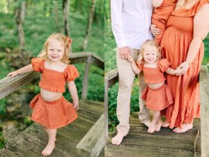 Young girl in an orange two-piece outfit smiling on a wooden bridge in a lush forest. Little girl holding hands with her parents on a bridge, with mom wearing a matching orange dress.