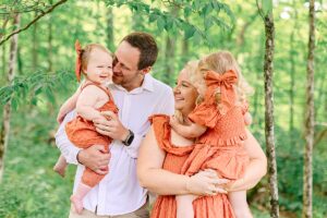 Family of four standing together in the forest, with both children in matching orange outfits.