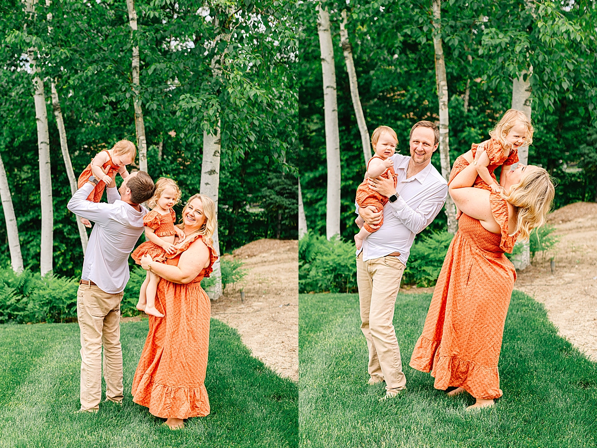 Side-by-side portraits of a couple smiling together, with mom wearing an orange dress in a green field. Parents lifting their daughters in the air while standing barefoot in front of birch trees.
