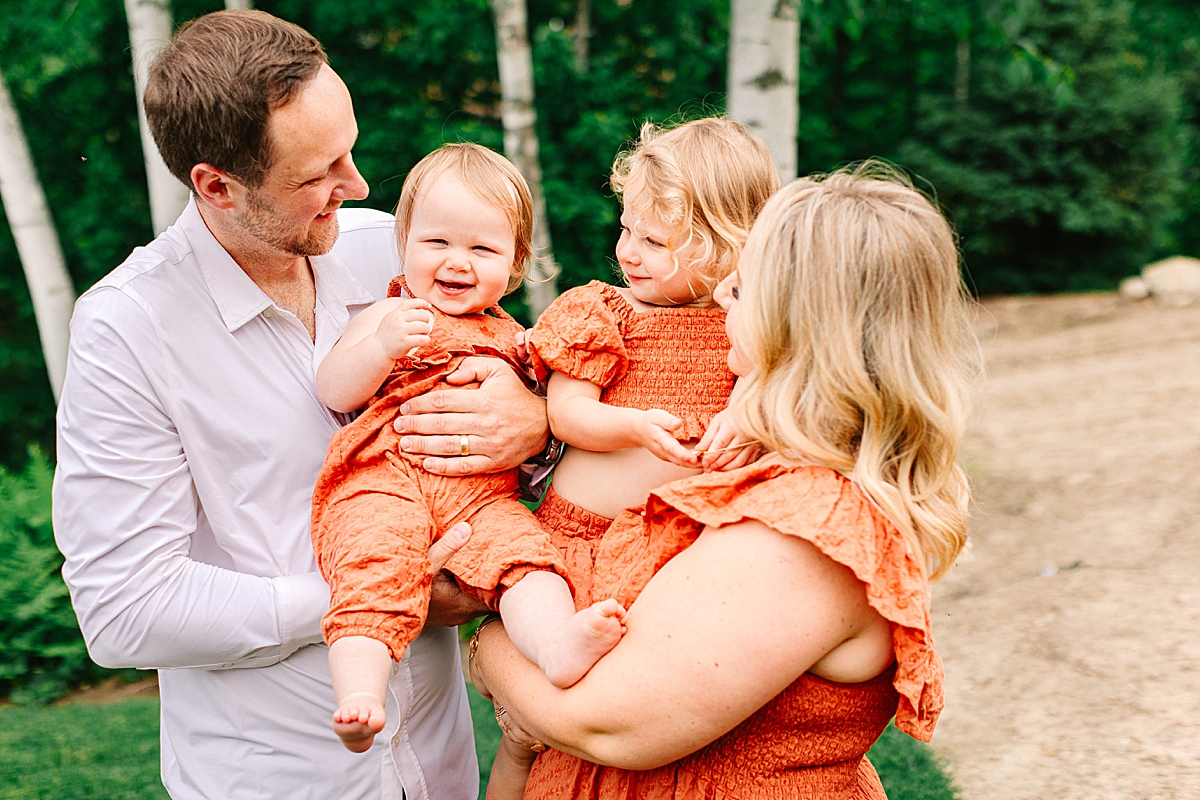 Baby girl smiling in her dad’s arms, with toddler and mom looking on happily.