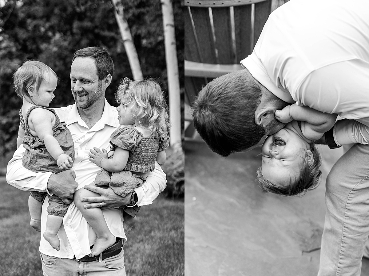 Black and white photo of dad holding both daughters in a park, all facing one another. Black and white image of dad bending down to kiss a laughing baby, who is playfully upside down.