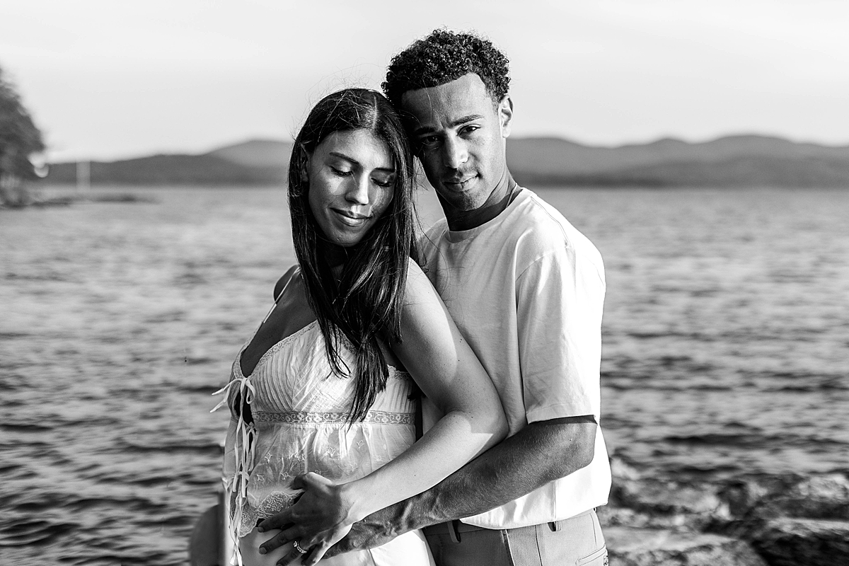 Black and white portrait of a couple standing close on a rocky dock, with the man's arms around the woman’s waist.
