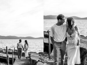 Black and white photo of a couple holding hands and walking on a dock, framed by mountains and lake views.