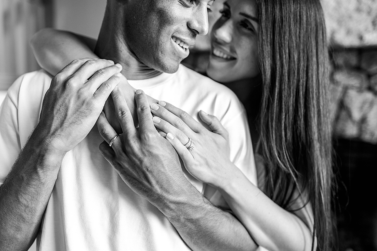 Black and white close-up of a couple embracing indoors, with their hands intertwined and wedding rings visible.